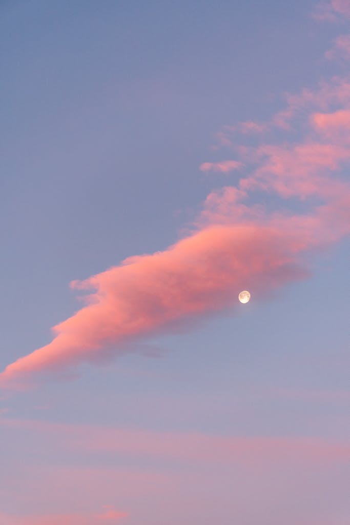 A tranquil sky with pastel pink clouds and a visible moon at twilight, perfect for calming backgrounds.